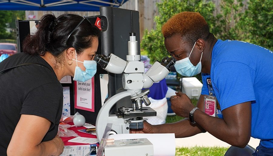 Pathology resident Adeyinka Akinsanya examines slides with a patient at Gennesaret Free Clinic’s See, Test & Treat event. 