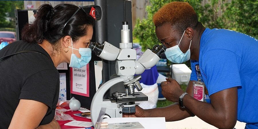 Pathology resident Adeyinka Akinsanya examines slides with a patient at Gennesaret Free Clinic’s See, Test & Treat event. 